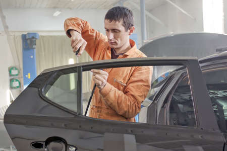 Auto service worker disassembles car door for repair, restoration.の写真素材