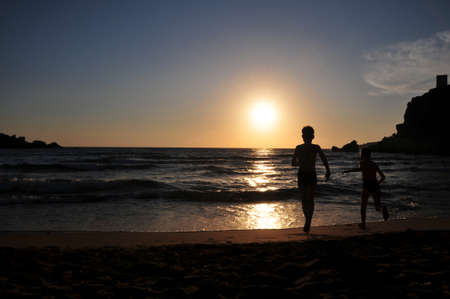 Boys running into sea during sunsetの写真素材