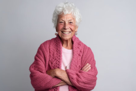 Portrait of a happy senior woman with arms crossed against gray backgroundの素材