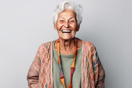 Portrait of a happy senior woman laughing while standing against gray backgroundの素材
