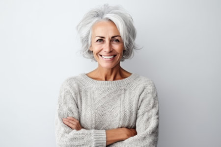 Portrait of a happy senior woman with gray hair standing with arms folded against white backgroundの素材