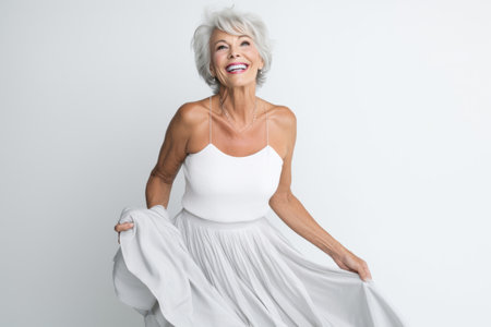 Portrait of happy senior woman in white dress posing against white backgroundの素材