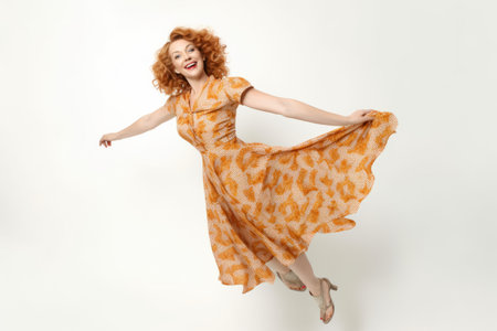 Full length portrait of a happy young woman with curly red hair jumping isolated over white backgroundの素材