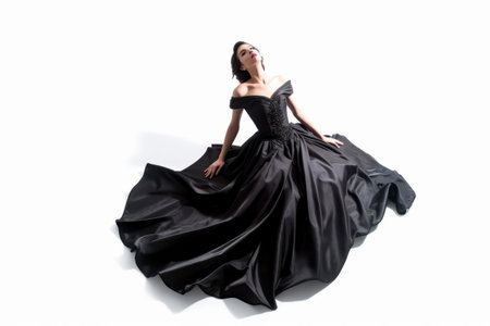 Young brunette woman in long black dress posing on white background.の素材