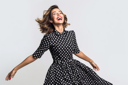 Cheerful young woman in polka dot dress dancing on white backgroundの素材