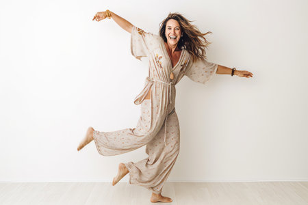 Full length portrait of happy woman in pajama jumping against white wallの素材