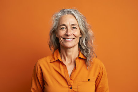 portrait of smiling senior woman looking at camera isolated on orange backgroundの素材
