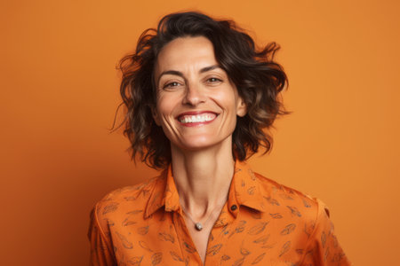 Portrait of a beautiful happy woman smiling at camera over orange backgroundの素材
