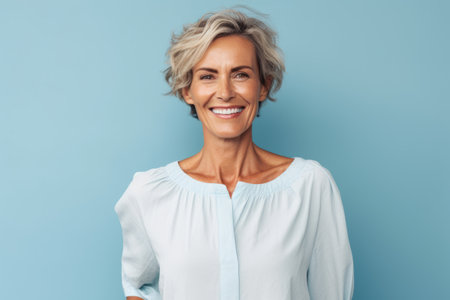 Portrait of smiling mature woman looking at camera isolated on blue backgroundの素材