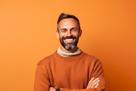 smiling middle aged man with crossed arms looking at camera isolated on orangeの素材