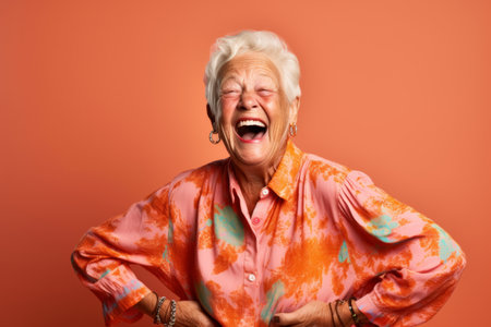 Portrait of a happy senior woman laughing. Isolated on orange background.の素材