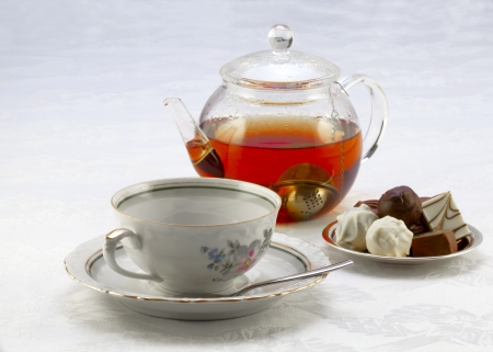 Cup on a saucer, teapot with tea and chocolates on a plateの写真素材