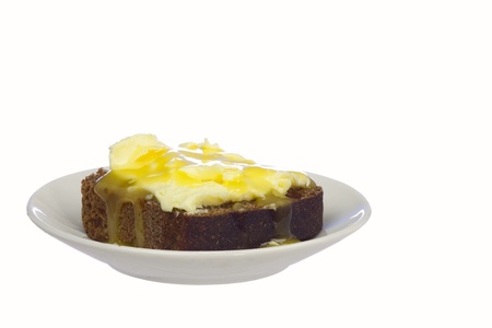 A piece of rye bread with butter and honey on a saucer, isolated on whiteの写真素材