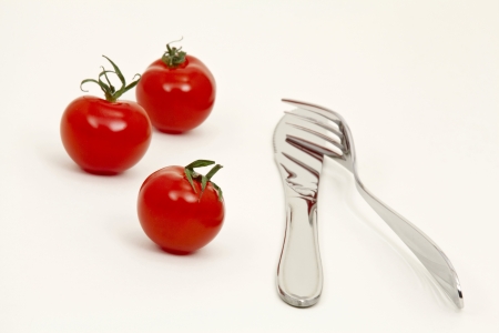 Red tomatoes, knife and fork on light backgroundの写真素材