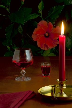 On the table a glass with red wine, a small glass with liquor and a burning candle in a candlestickの写真素材