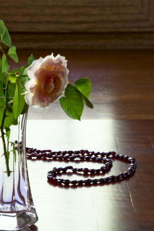 Garnet necklace and a rose in a glass vase on an old tableの写真素材