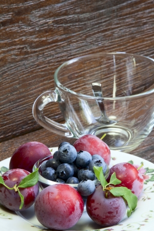 Teacup and ripe plums and blueberries on a wooden backgroundの写真素材
