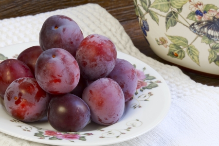 Ripe plums on a white plate with a floral ornamentの写真素材