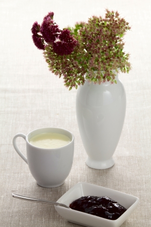 A cup of milk plam jam and autumn flowers in a vaseの写真素材