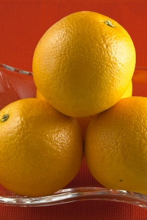 Ripe oranges in a glass vase on a red backgroundの写真素材