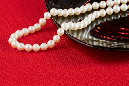 Pearl necklace and black ceramic dish on a red tableclothの写真素材