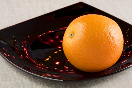 Ripe orange on a black ceramic dish among the reflections of lightsの写真素材