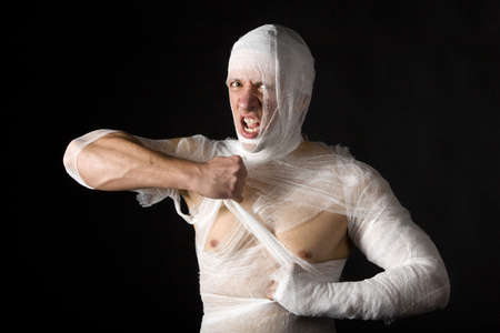 Studio image of a young man bandaged, on black background. Concept for health-care or ancient mummyの写真素材
