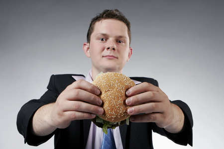 Businessman holding a hamburger. Selective focus. Focus is on the burger.の写真素材