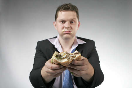 Unhappy businessman holding a hamburger. Focus is on the burger.の写真素材