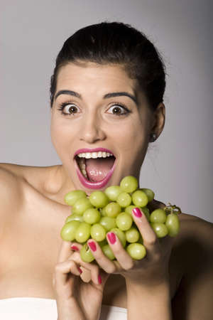 Part of photo series of a woman enjoying fresh green grapes. Studio shotの写真素材
