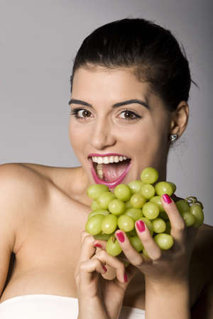 Part of photo series of a woman enjoying fresh green grapes. Studio shotの写真素材