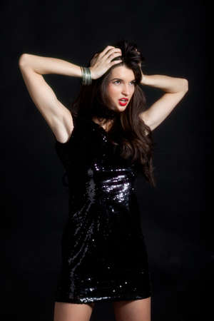 Sexy young woman posing in sequin dress, looking away. Studio image, on black backgroundの写真素材