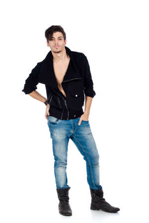 Handsome young fashion model standing and wearing jeans, boots and a black jacket. Isolated on white background. Studio vertical image.の写真素材