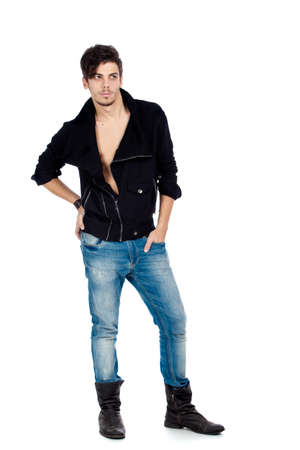 Handsome young fashion model standing and wearing jeans, boots and a black jacket. Isolated on white background. Studio vertical image.の写真素材