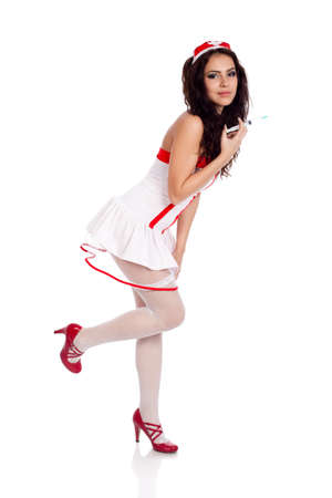 Full body shot of a sexy beautiful young nurse wearing red high heels shoes holding a syringe on isolated white background. High resolution studio image with copy space for text.の写真素材