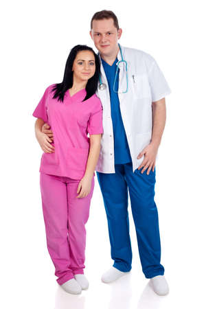 Young smiling couple of handsome man doctor and pretty nurse in blue and pink scrubs uniforms, looking at camera. Full body image, isolated on white background. High resolution in studio, part of healthcare concept series.の写真素材