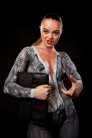 View of a sensual naked woman covered in body paint reperesenting office suit, holding a paper case and looking at camera. High resolution concept image in studio on black backgroundの写真素材