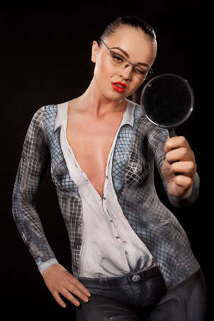 Naked shocked woman covered with body paint representing business suit, holding a magnyfing glass. Concept image of sexual issues at work. High resolution studio picture on black background.の写真素材