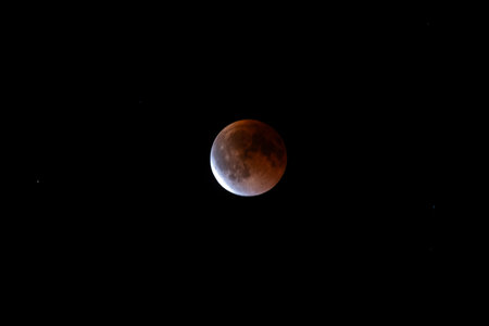 Partial lunar eclipse with copper moon and bright sunlit limb on black sky