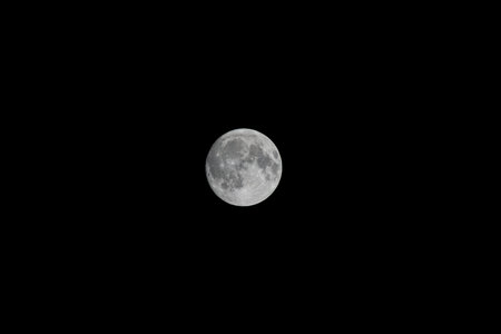 A wide telephoto shot of the full moon over a subtle night landscape, captured with a shorter focal...
