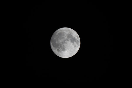 A dramatic photo of the full moon captured with a longer telephoto lens, showing extreme details of...