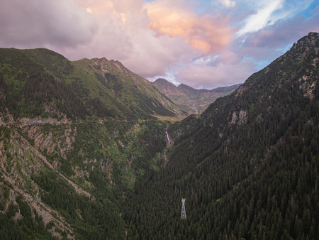 Aerial view of alpine valley with waterfall and evergreen forest at sunsetの写真素材