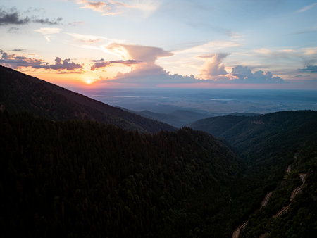 Sunset over winding road through mountain forest valley, aerial drone viewの写真素材