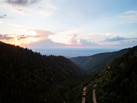 Aerial drone view of forested mountain valley at sunset with winding roadの写真素材