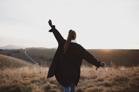 young woman in running up on top of mountain summit at sunset ,, raises arms into air, happy and...