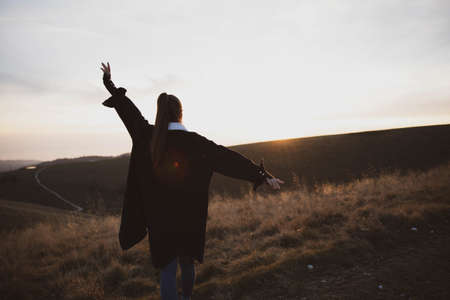young woman in running up on top of mountain summit at sunset ,, raises arms into air, happy and drunk on life, youth and happinessの写真素材