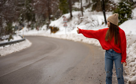 Young beautiful girl catches the car on the winter road in the forestの写真素材