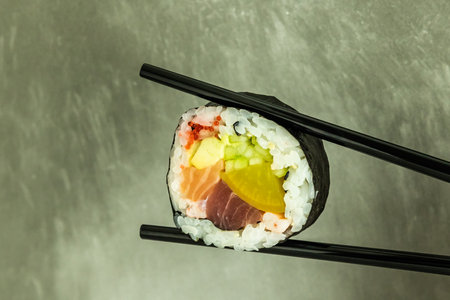Hand holding sushi roll using chopsticks on gray background. Japanese foodの写真素材