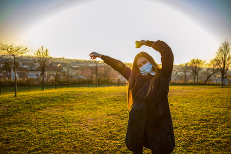 Girl with hands in the air and protective mask. in the park at sunsetの写真素材