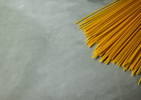 Yellow long spaghetti on gray background. Thin pasta arranged in rows. Yellow italian pasta. Long...